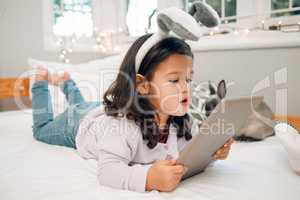 Watching this show for hours. an adorable little girl lying on her bed with a digital tablet.