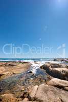 Big rocks in the ocean under a clear blue sky with copy space. Beautiful landscape of beach waves, tides and currents flowing through boulders and big stones in the sea on a calm, bright summer day