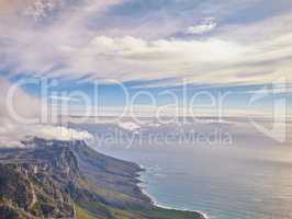 Aerial view of a calm ocean and mountains with a blue cloudy sky background and copy space. Stunning nature landscape of the sea and horizon from Table Mountain tourism destination in Cape Town