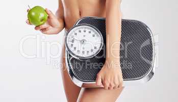 Being healthy means feeling good about the choices Im making. a healthy young woman holding an apple and a weight scale.