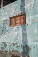 Architecture of an old blue wall with peeling paint outside. Exterior texture details of an old rustic residential build with vintage wooden shut windows discovered in Santa Cruz de La Palma