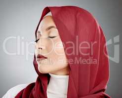 Stylish young muslim woman in a red hijab with her eyes closed on a grey studio background. Middle eastern woman wearing makeup and a headscarf while feeling calm and showing the beauty in modesty