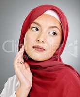 A glowing beautiful muslim woman isolated against grey copyspace background. Young woman wearing a hijab or headscarf showing her eyelash extensions while daydreaming, touching her flawless skin