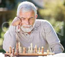 Where should I move next. a senior man sitting alone outside and looking contemplative while playing a game of chess.