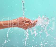 Nothing tastes as good as skin feels. an unrecognisable woman cupping her hands to catch water against a blue background in the studio.