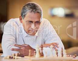 My opponent is really good. a mature man sitting alone inside and looking contemplative while playing a game of chess.