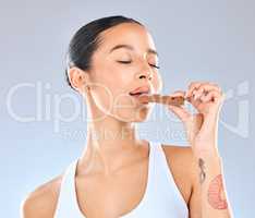 Why does bad taste this good. Studio shot of a young woman enjoting a bite of chocolate against a grey background.