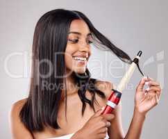 Youre beautiful just as you are. a young woman using a curling iron against a grey background.