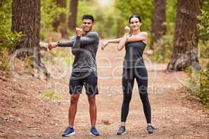 Portrait of a happy young male and female athlete stretching their arms before a run outside in nature. Two fit sportspeople doing warm-up exercises in pine forest on a sunny day