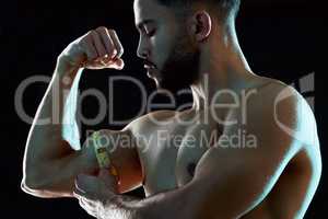 Gains like these dont grow on trees. Studio shot of a fit young man measuring his bicep against a dark background.