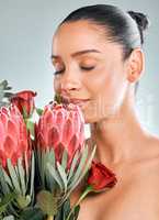 A fragrance scent from heaven. Studio shot of an attractive young woman smelling protea flowers against a grey background.