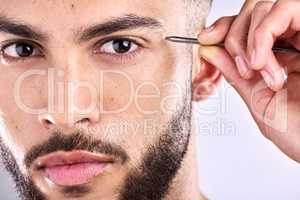 Im serious about looking my best. Closeup shot of a young man plucking his eyebrows against a grey background.