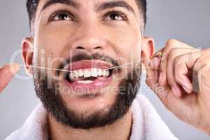 Everyone knows how to get a bright smile. a young man flossing his teeth while standing against a grey background.