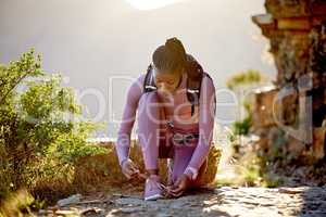 Young african american woman tying the laces of her sneakers for exercise outdoors. One female only fastening and tightening her shoes to prevent tripping while exploring nature on a hiking trail