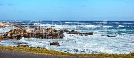 Stunning blue ocean coast with a clear sky background and copy space. Beautiful sea water splashing against rocky shore under bright summer sky. Open and empty nature landscape or seascape with waves