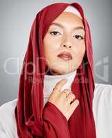 Portrait of a Muslim woman wearing a red hijab or headscarf showing her eyelash extensions and makeup. Showing her flawless skin glowing. Beautiful woman isolated against a grey studio background.