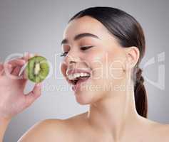 Its packed with antioxidants. Studio shot of an attractive young woman posing with half a kiwi against a grey background.