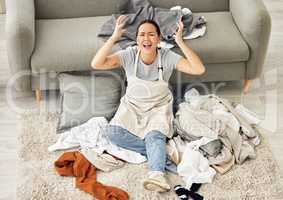 One mixed race woman sitting in a pile of messy laundry and having a mental breakdown in the living room. A young Asian woman feeling overwhelmed and in need of help with housework