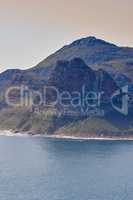 A mountain in the ocean at Hout Bay, South Africa on a summer day. Sea tropical landscape or Mediterranean seascape on a hot afternoon. Wild coast beach scenic view as holiday or vacation destination