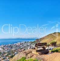 Beautiful aerial view of empty bench overlooking city and ocean in Cape Town, South Africa against blue sky copyspace. A calm sunny day with a park chair on a cliff, with scenic views and fresh air