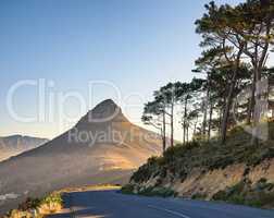 Beautiful view of mountain named Lions Head on sunny Summer day. Nature around includes green trees ahead with road beside to enjoy drives. Area is in Cape Town in the Western Cape of South Africa.