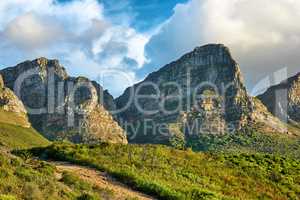 Landscape of a mountain in Cape Town, South Africa in the day. Rocky mountaintop with greenery against cloudy sky. Below of popular tourist attraction and adventure hiking trail near table mountain