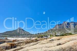 Landscape of mountains and moon on blue sky with copy space. Beautiful rock outcrops of mountaintops near the coastline or bay area. View of Devils Peak and Table Mountain in Cape Town, South Africa