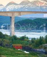 Landscape view of Saltstraumen Bridge in Nordland, Norway in winter. Scenery of transport infrastructure over a river or stream with a snow-capped mountain background. A remote cabin overseas