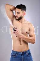 If you smell good, you feel good. Studio shot of a handsome young man spraying deodorant on his armpit.