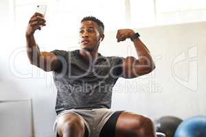 These guns are worth bragging about. a muscular young man taking selfies while exercising in a gym.