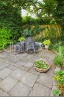 A view of the garden backyard of a house with an artistic chair, wooden bench, and a variety of plants, trees, and shrubs on a yard. Inside in a formal elegant garden setting on early summers day.