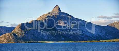 Scenic view a mountain lining a coast in Bodo, Norway. An expansive natural vista of a spring lake during sunrise in the morning. Remote, lush vegetation alongside a lake in a European destination