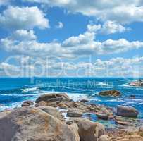 Rocks in the ocean under cloudy blue sky background with copy space. Beautiful landscape of beach waves splashing against boulders or stones in aqua sea water. Summer nature location in South Africa