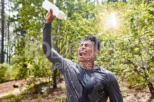 Young mixed race hispanic fit male athlete refreshing himself with water while on a run in a forest outside in nature. Exercise is good for health and wellbeing. Resting after a workout