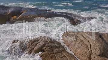 Scenic ocean view of beach with rocks or boulders and sea water washing onto shore during peaceful summer vacation in tropical resort and island overseas. Rough texture and detail of rocky coastline