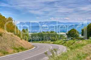 Scenic countryside route on a sunny day in Summer. Empty curved road with a beautiful view of nature, and a background landscape of the farmlands, mountains and cloudy blue sky.