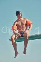 Chilling at the top. Full length shot of a handsome young male athlete sitting on a diving board outside.