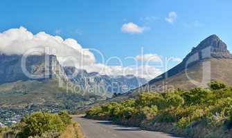 A road along a mountain and green nature with a cloudy blue sky and copy space. Beautiful landscape of a peaceful tarred roadway near plants and the wilderness on a summer day