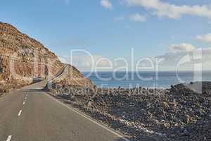 Tar road or street leading to scenic mountains with sea view during summer roadtrip in La Palma, Canary Islands, Spain. Landscape of a rocky ocean mountain pass with blue sky, clouds and copy space