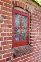 Old dirty window in a red brick house or home. Decaying casement with redwood frame on a historic building with clumpy paint texture. Exterior details of a windowsill in a traditional town or village