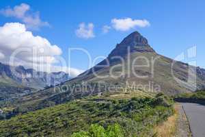 Lions Head mountain and green, natural landscape in Cape Town, South Africa. Outdoor hiking spot with blue sky backdrop and plants by a road. Beautiful view of nature while traveling.