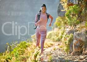 Young fit and active african american woman hiking and jogging through the mountains on a sunny summer day. Black woman running alone exercising and carrying a backpack while exploring nature looking determined and focused while wearing her sportswear out