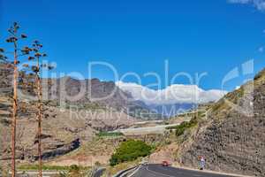 Beautiful landscape of a countryside tar road with a cloudy blue sky and copy space. Roadway with cars driving to holiday destination through the mountains in Spain on a summer afternoon or day