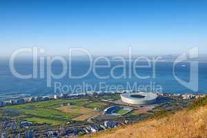 Above panoramic photo of a the central business district of Cape Town, Western Cape, South Africa. A busy peninsula where land meets sea against a cloudscaped blue sky. A beautiful mountainside city