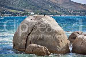 Big rocks in the blue ocean with mountains in the background. Stunning nature landscape or seascape on a summer day. Boulders or large natural stones in aqua sea water with beautiful rough textures