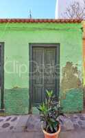 Old abandoned house or home with a weathered green wall and aging wooden door. Vintage and aged residential building built in a traditional architectural style or design with a cobble stone road