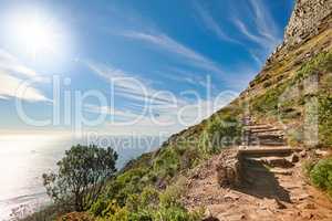 Copy space with scenic coast and rocky mountain slope with cloudy blue sky background. Rugged landscape of plants growing on a cliff by the sea with hiking trails to explore in Cape Town South Africa