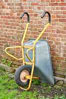 Wheelbarrow against the side of a red brick wall or house. Doing gardening or cleanup work in a backyard garden on a sunny day. Professional landscapers use this equipment to move soil or dirt
