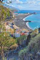 Landscape of an ocean coast with black beach sand on Puerto de Tazacorte. Colorful town houses or holiday resort accommodation near the seaside in a beautiful tourism destination, La Palma, Spain