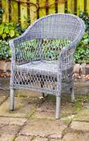 Rattan armchair in a garden patio or terrace on a sunny day in autumn. Rustic outdoor furniture in a calm and peaceful environment surrounded by nature. Cosy spot to enjoy a break with fresh air